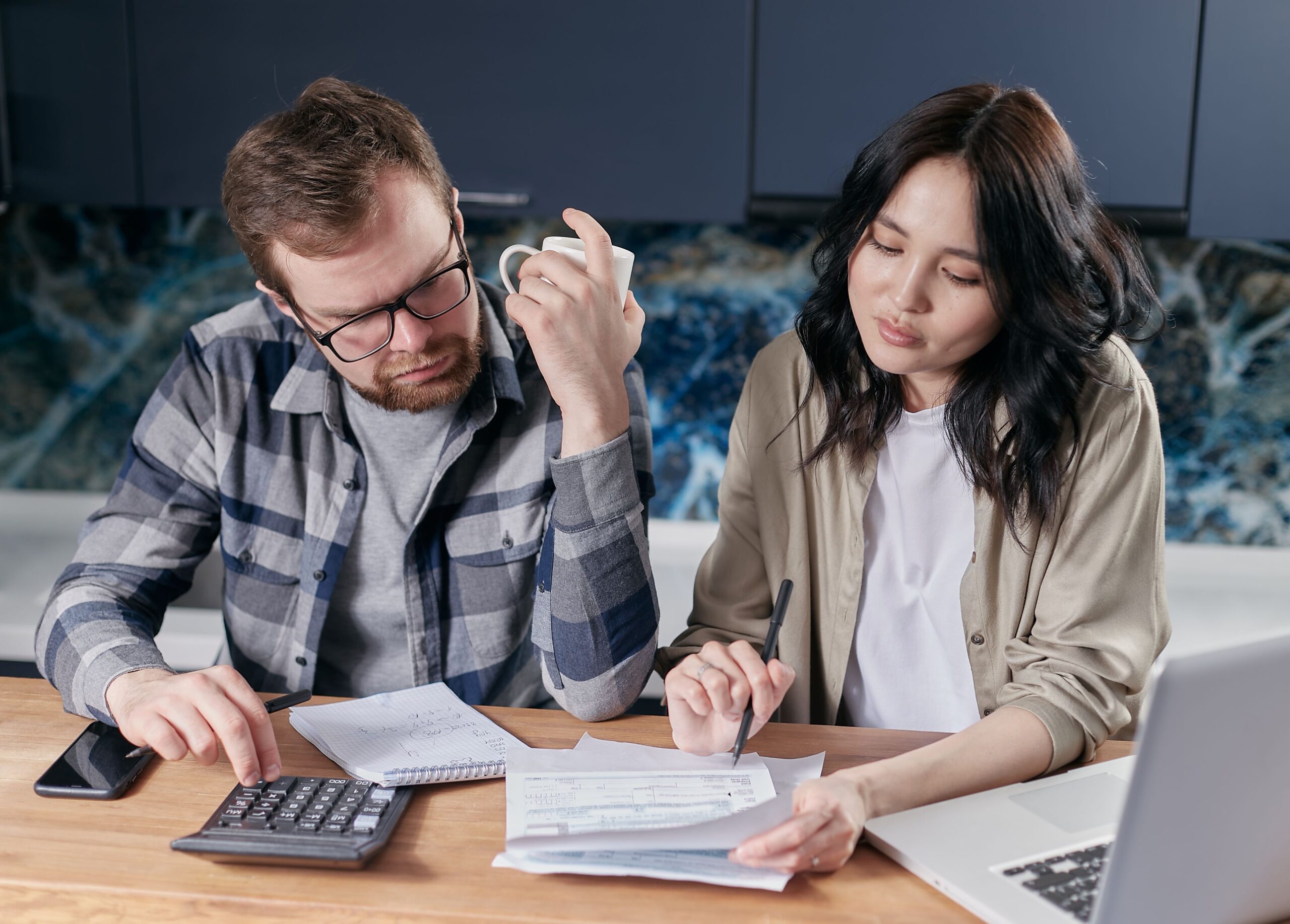 Older married couple reviewing financial documents and a calculator at their kitchen table
